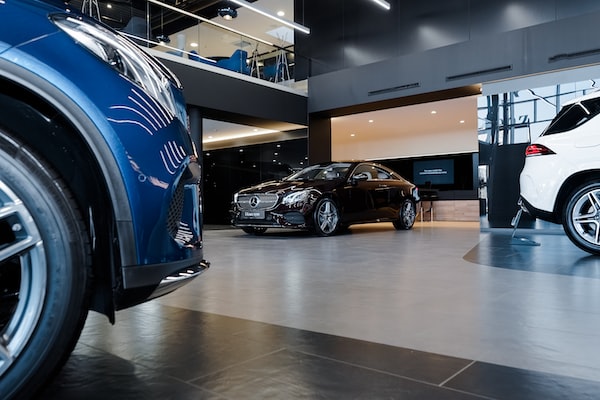 several differently colored cars are displayed in a showroom, including a black Mercedes