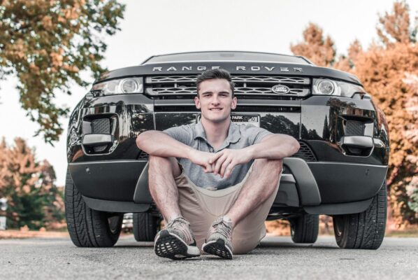 A young man poses for a picture with his new car purchase