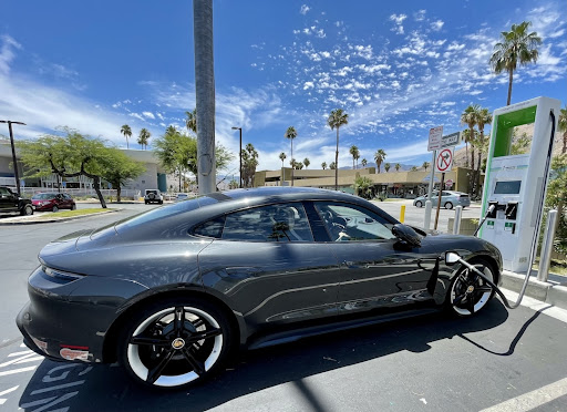 A charcoal-colored electric sedan is plugged into an EV charging port in a parking lot.